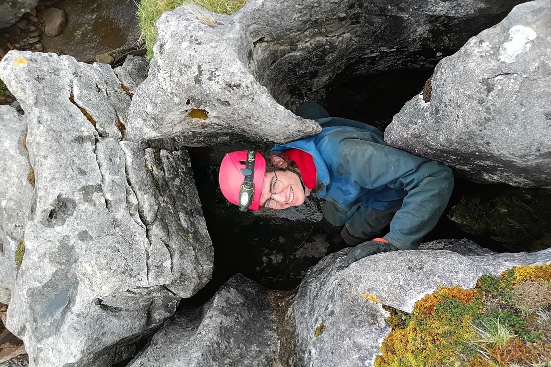 Mann mit rosa Helm und Stirnlampe klettert in engen Felsen mit Moos bei Caving-Abenteuer