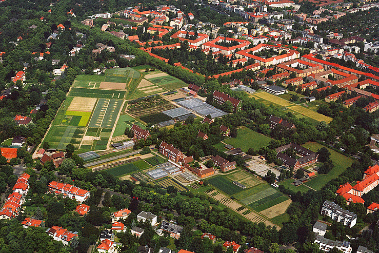 Eine Luftaufnahme auf den Campus Dahlem. Man sieht zahlreiche Felder, Gewächshäuser und Backsteingebäude. 