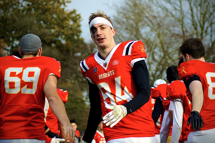 Mehrere Footballspieler in roten Trikots mit weißen und schwarzen Details stehen auf einem Spielfeld im Freien.