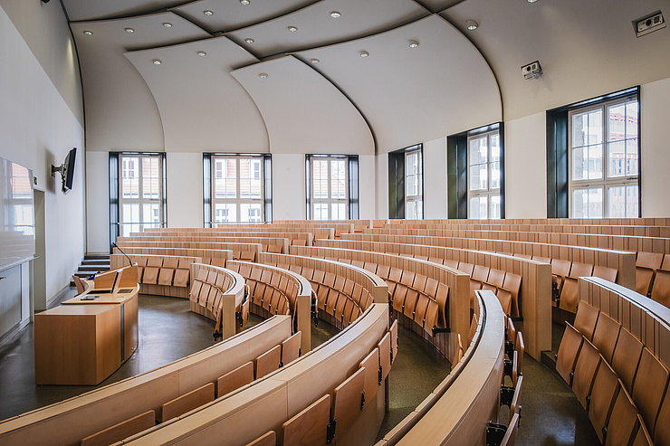 Ein moderner Hörsaal mit Holzsitzbänken die in halbrunder Form angeordnet sind