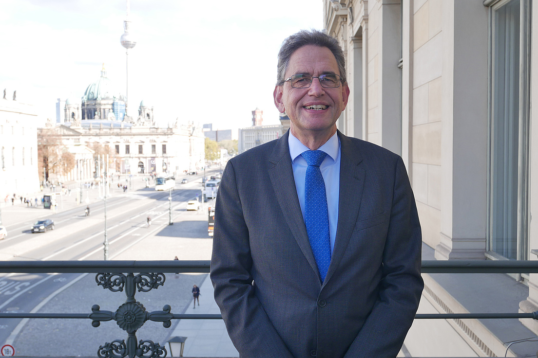 Matthias Ruffert steht auf einem Balkon. Im Hintergrund ist die Straße Unter den Linden, die Humboldt-Universität, der Berliner Dom und der Fernsehturm zu sehen,