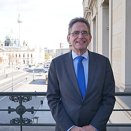 Matthias Ruffert steht auf einem Balkon. Im Hintergrund ist die Straße Unter den Linden, die Humboldt-Universität, der Berliner Dom und der Fernsehturm zu sehen,