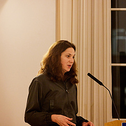 Portrait Viktoria Tkaczyk Viktoria Tkaczyk steht hinter einem Rednerpult und spricht ins Mikrofon anlässlich der Verleihung des Caroline von Humboldt-Preises. Sie trägt einen dunkelfarbenen Overall.