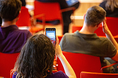 Person, die aus dem Publikum ein Foto mit dem Telefon vom Podium macht