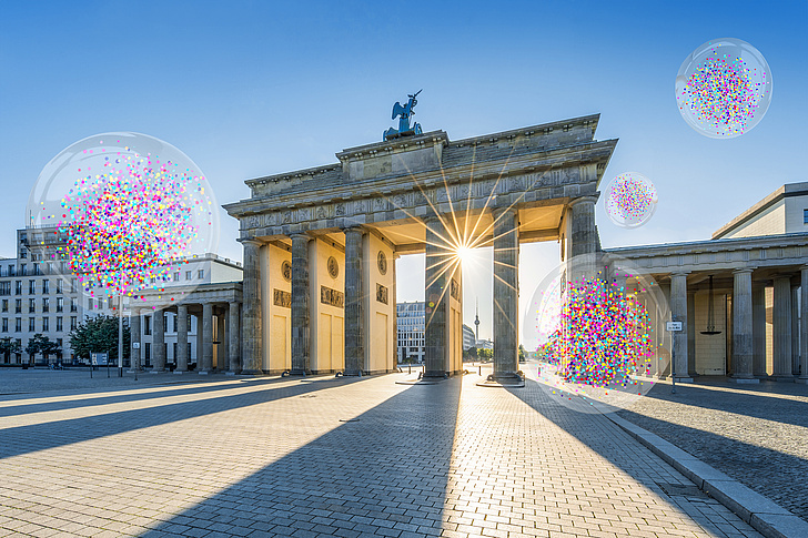 Ein Bild vom Brandenburger Tor, im Hintergrund blauer Himmel und Sonnenstrahlen, die zwischen den Säulen hervorscheinen. Im Bild sind auch vier transparente Blasen mit Konfetti zu sehen. 