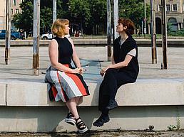 Charlett Wenig und Johanna Hehemeyer-Cürten sitzen sich auf einer Betonbank gegenüber