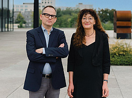 Prof. Dr. Andrew James Johnston und Prof. Dr. Anne Eusterschulte  stehen vor der Neuen Nationalgalier auf der Besucherterasse der Galerie