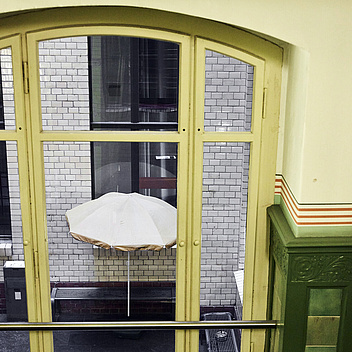 Eine Glastür zu einem kleinen Innenhof, in dem ein kleiner Sonnenschirm und Bänke stehen.