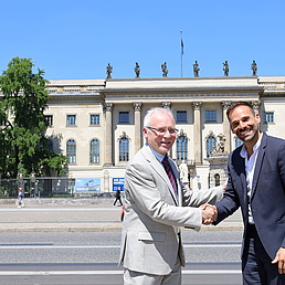 Two men shake hands in front of the main building of HU.