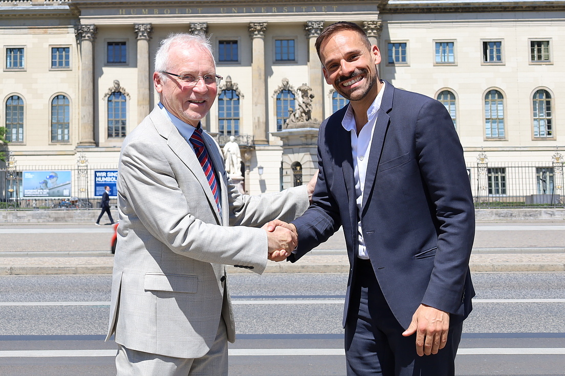 Two men shake hands in front of the main building of HU.
