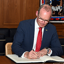 Simon Coveney sitzt am Tisch und schreibt in ein vor ihm ausgebreitetes Buch.
