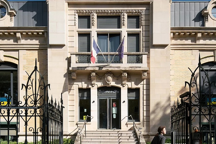 Eingangsgebäude der Sciences Po Dijon mit Fassade, Treppen und schmiedeeisernem Tor unter blauem Himmel.