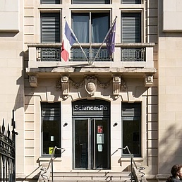 Eingangsgebäude der Sciences Po Dijon mit Fassade, Treppen und schmiedeeisernem Tor unter blauem Himmel.