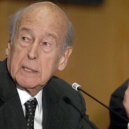Valery Giscard d'Estaing schaut zur Seite. Vor ihm ist ein Mikrofon, in das er zu sprechen scheint.