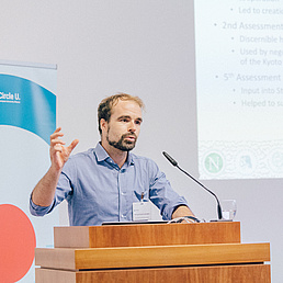 Foto eines Mannes, der hinter einem Rednerpult einen Vortrag hält