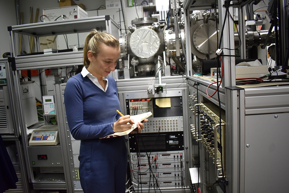 Eine Frau in einem Raum voller verschiedener Geräte schreibt etwas auf einen Zettel.