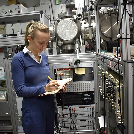Eine Frau in einem Raum voller verschiedener Geräte schreibt etwas auf einen Zettel.