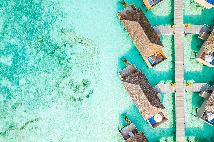 Stelzenhäuser im türkisen Wasser der Malediven, von oben fotografiert