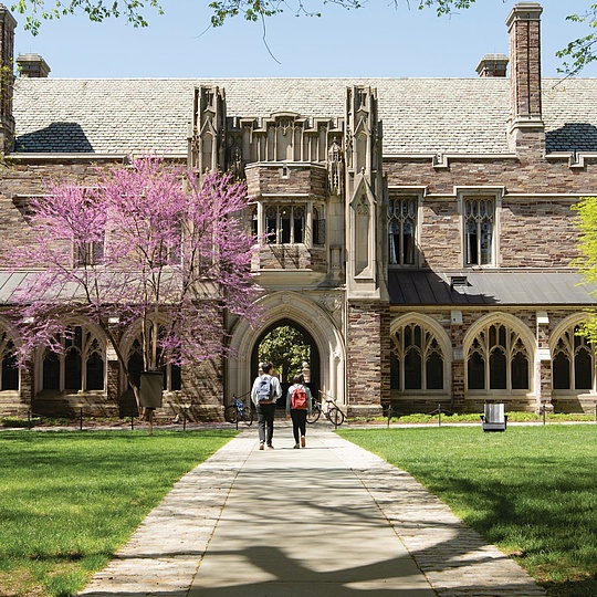 Zwei Personen, die auf einem von einem Rasen umschlossenen Weg auf ein Gebäude zugehen.