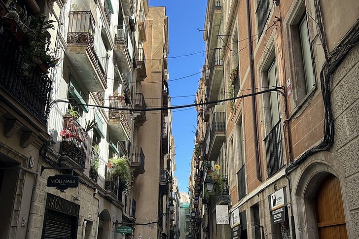 Enge Gasse mit mehrstöckigen Wohnhäusern auf beiden Seiten und blauem Himmel darüber