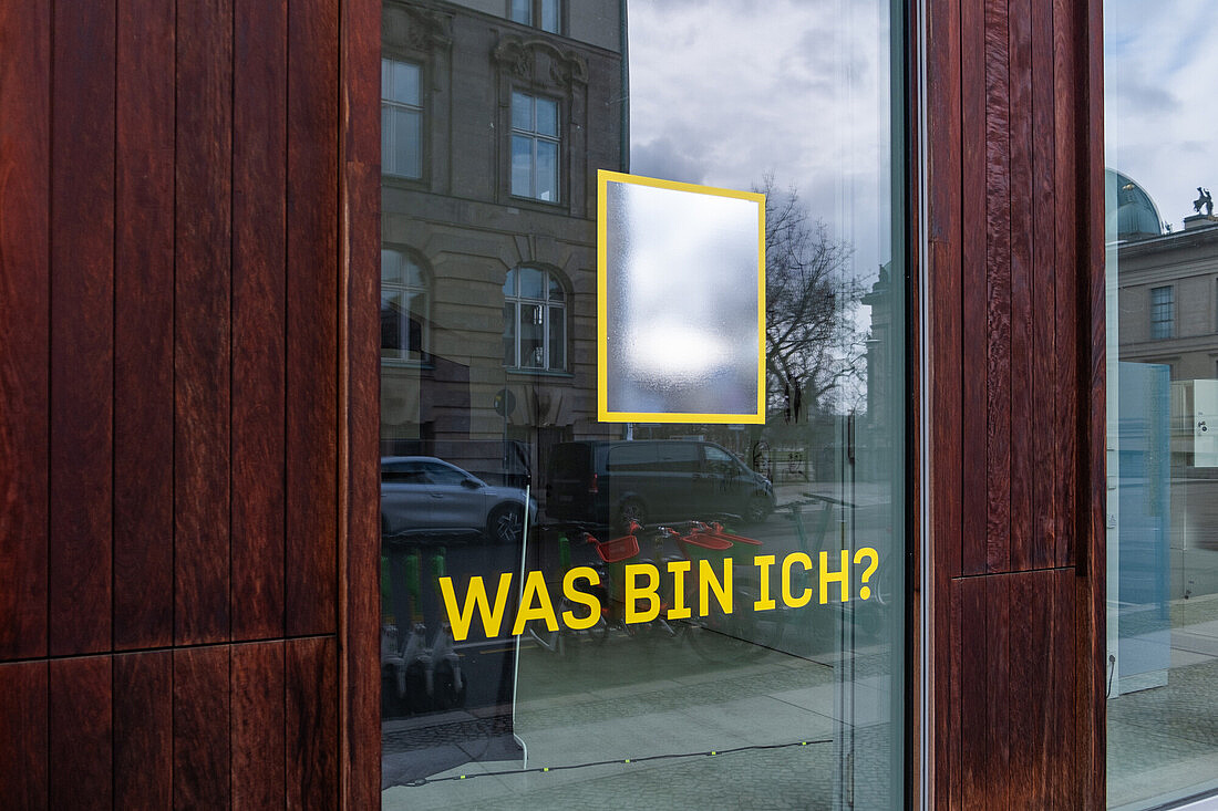 Glastür mit Holzrahmen mit der Aufschrift "Was bin ich"