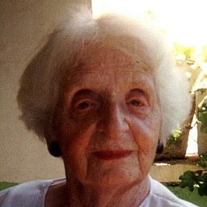 Gerda Wolfsohn-Zondek in einem Zimmer am Fenster sitzend. Sie schaut in die Kamera und trägt einen weißen Pullover mit blauer Blume. Ihr Haar ist kurz und weiß.