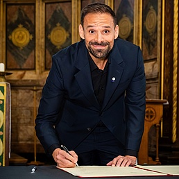 A man signs an agreement in a ceremonial hall
