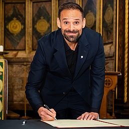 A man signs an agreement in a ceremonial hall
