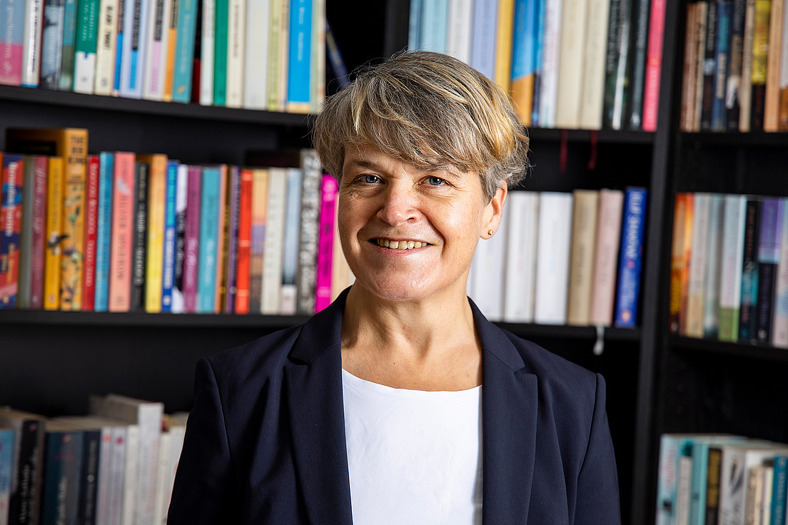 Sociologist Talja Blokland with short hair, white top and dark blazer in front of a bookcase filled with books