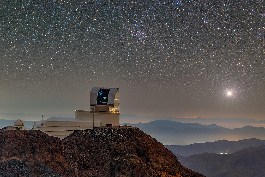 Auf dem Berggipfel El Peñón in den chilenischen Anden befindet sich das Vera C. Rubin Observatory mit geöffneter Kuppel bei Nacht mit klarem Sternenhimmel im Hintergrund.