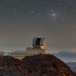 Auf dem Berggipfel El Peñón in den chilenischen Anden befindet sich das Vera C. Rubin Observatory mit geöffneter Kuppel bei Nacht mit klarem Sternenhimmel im Hintergrund.