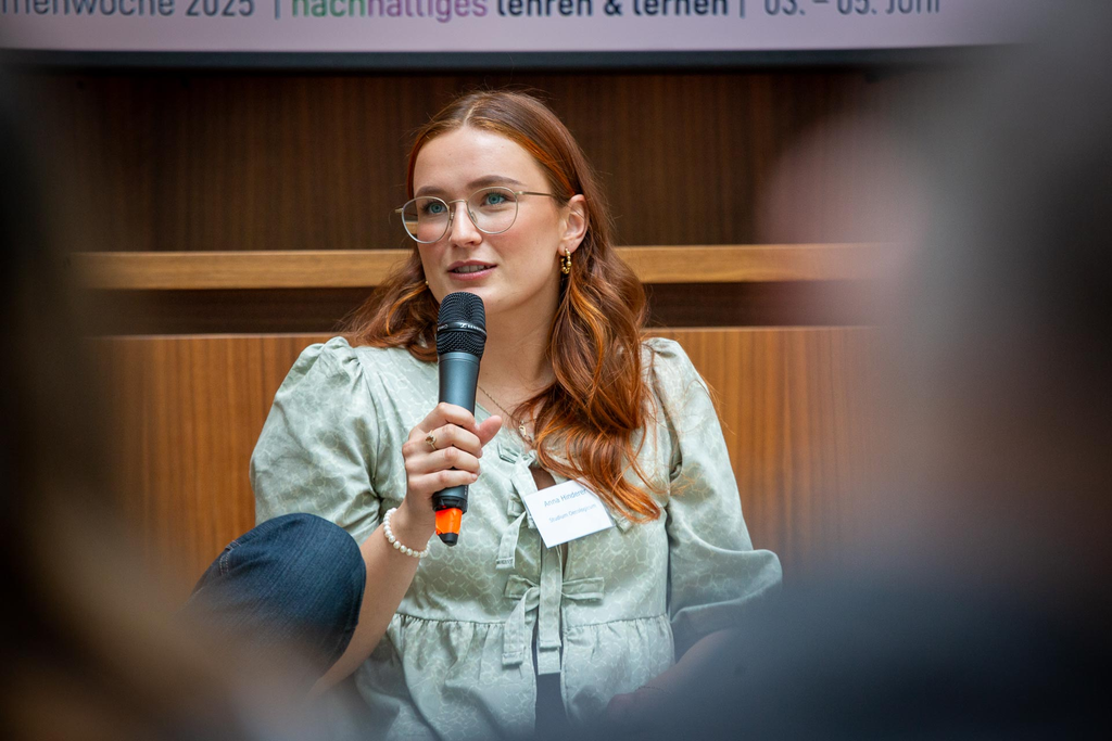 Anna Hinderer sitzt auf einem Stuhl und spricht ins Mikrofon, das sich in ihrer Hand befindet.