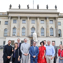 A group of women and men pose for a photo in front of the façade of the HU's main building.