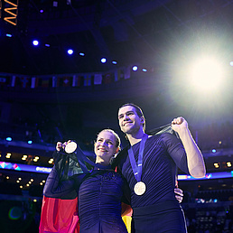 Eispaar mit Goldmedaillen und deutscher Flagge auf dem Podium.
