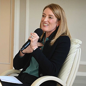 Roberta Metsola lachend mit einem Mikrofon in der Hand, dem Publik zugewandt.