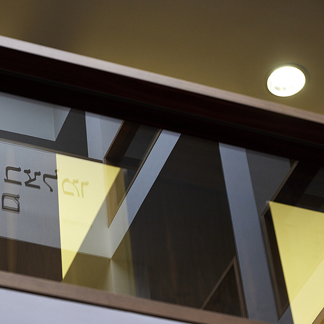 Das Bild zeigt eine mit Glas verzierte Holzwand, in der sich Buchstaben des hebräischen Alphabets spiegeln.