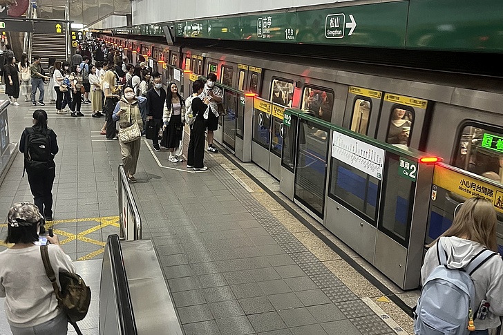 Menschen stehen auf einem Bahnsteig neben einem einfahrenden Zug in einer U-Bahn-Station mit grüner Beschilderung.