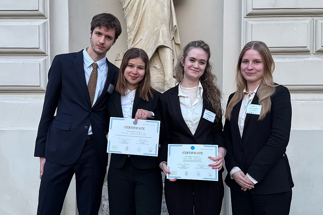 Photo of three young women and a young man in smart business attire showing off their winner's certificates.