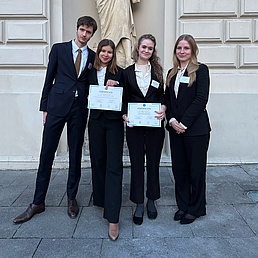 Foto von drei jungen Frauen und einem jungen Mann in eleganter Berufskleidung, die ihre Siegerurkunde vorzeigen.