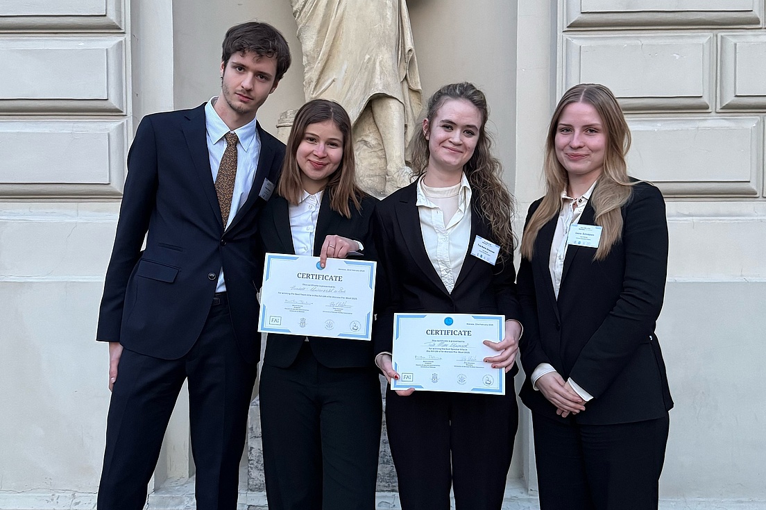 Foto von drei jungen Frauen und einem jungen Mann in eleganter Berufskleidung, die ihre Siegerurkunde vorzeigen.