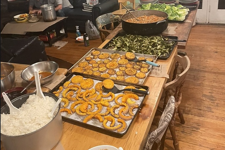 Küchentisch mit mehreren Backblechen gefüllt mit gebackenen Kürbisscheiben und -ringen, einem Topf mit Reis, einer großen Schüssel mit Salat und einem Topf mit einer anderen Speise.